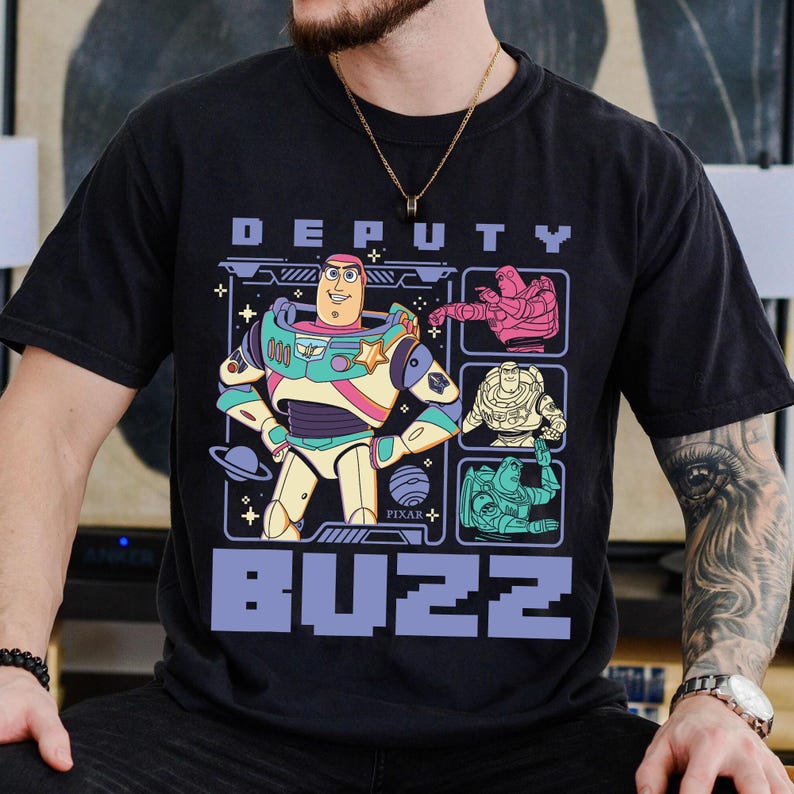 May include: Black t-shirt featuring a graphic of Buzz Lightyear from the Pixar movie Toy Story. The design includes the words "DEPUTY BUZZ" in pixelated font, and images of Buzz in different poses. The shirt has a crew neck and short sleeves.