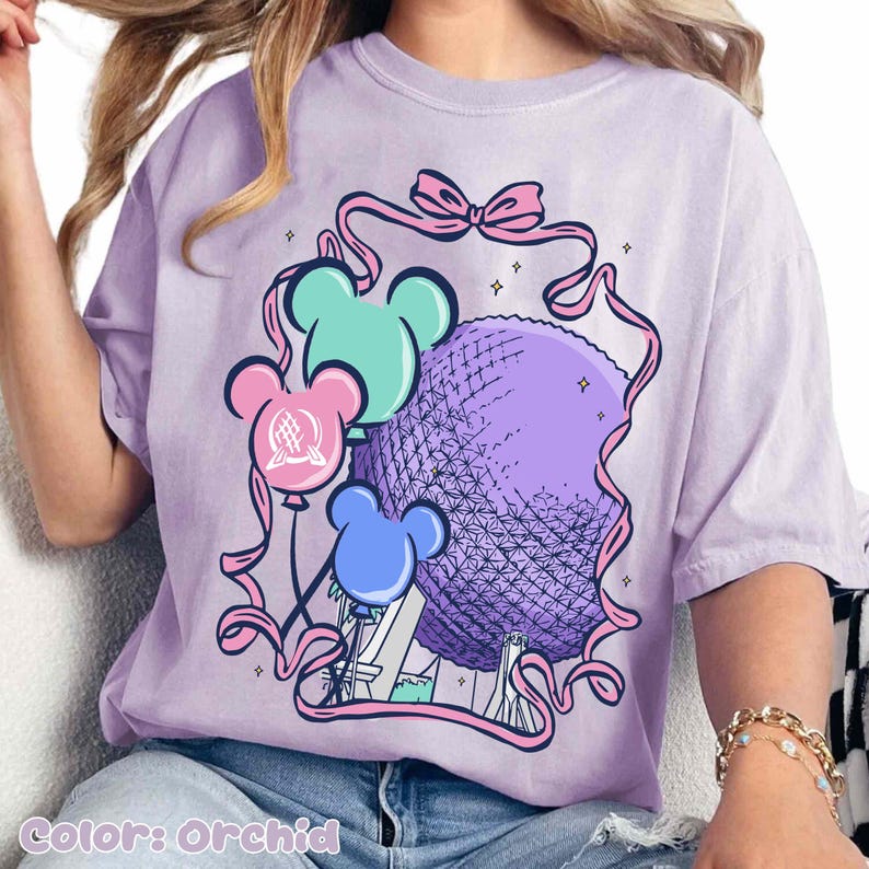 May include: Orchid-colored t-shirt featuring a graphic of Mickey Mouse-shaped balloons in teal, pink, and blue, with a large purple sphere and pink ribbon accents. The text "Color: Orchid" is at the bottom.