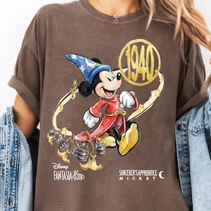 May include: Brown t-shirt featuring a graphic of Mickey Mouse in Sorcerer's Apprentice attire. The design includes the text "Disney Fantasia 85th" and "1940". Mickey is depicted in a red robe and blue hat.