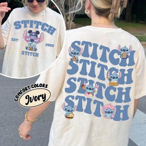 May include: Ivory-colored t-shirt featuring the word "STITCH" in blue, along with a cartoon character wearing sunglasses. The back of the shirt repeats "STITCH" in blue with Stitch character graphics. The shirt is from Comfort Colors.