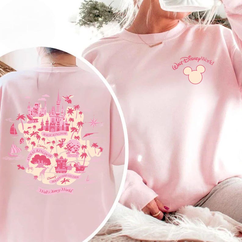 May include: A light pink sweatshirt featuring a Walt Disney World design. The front has the words "Walt Disney World" and a Mickey Mouse head. The back displays a map of Disney World attractions in pink and white.