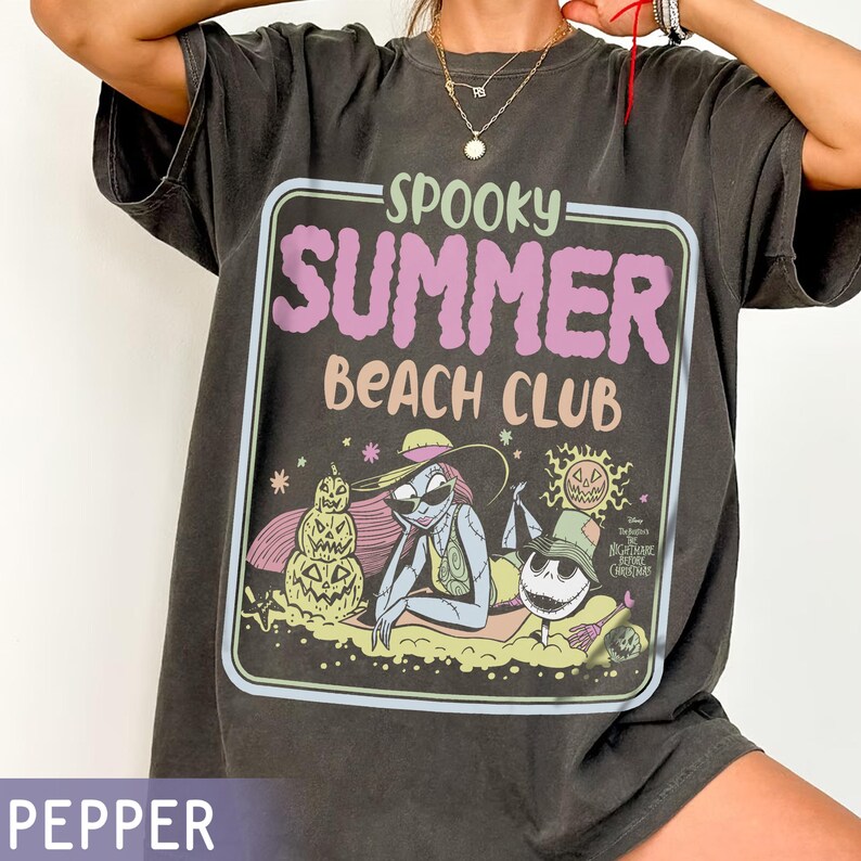 May include: Dark gray t-shirt with a graphic that reads "Spooky Summer Beach Club." The graphic features characters from The Nightmare Before Christmas, including Sally and Jack Skellington, in a beach setting. The shirt is a relaxed fit.