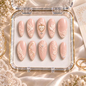 May include: A set of ten almond-shaped press-on nails in a soft blush pink base color. The nails feature intricate white 3D relief designs including doves, floral vines, lace patterns, and a central heart emblem with the letters A and J.