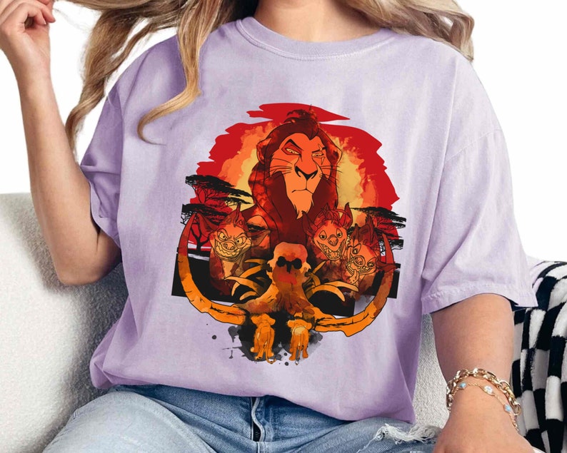 May include: A purple t-shirt with a graphic print of Simba, the lion from Disney's The Lion King, with a sunset background and hyenas in the foreground.