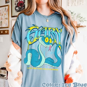 Op de afbeelding: Ijsblauw T-shirt met een cartoon slang en het woord "GARY" in een gestileerd lettertype. De slang is lichtblauw met gele accenten en een roze tong. De tekst "LIFE ON THE WILD SIDE" staat eronder.