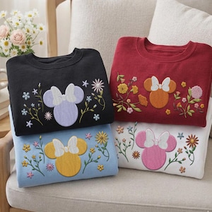 Pu&ograve; includere: Quattro felpe girocollo in nero, rosso, azzurro e bianco. Ognuna presenta una silhouette ricamata di una testa di topo con un fiocco, circondata da vari steli floreali colorati e piccoli fiori cuciti sulla parte anteriore del petto.
