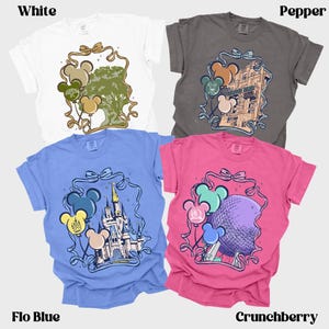 May include: Four t-shirts in white, pepper, flo blue, and crunchberry. Each shirt features a unique graphic within a decorative frame, including Mickey Mouse balloons. The shirts are short-sleeved and have the color names printed at the bottom.