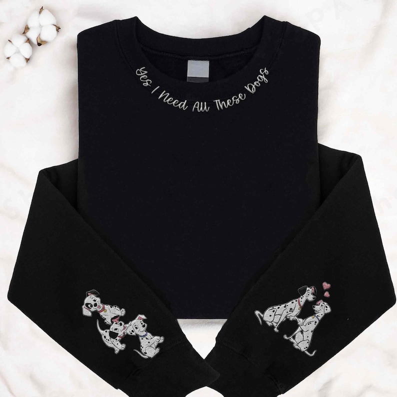 Op de afbeelding: Zwart sweatshirt met de tekst "Ja, ik heb al deze honden nodig" geborduurd op de halslijn. De mouwen hebben geborduurde afbeeldingen van Dalmati&euml;rs.
