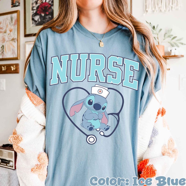 May include: Ice blue t-shirt with the word "NURSE" in light blue block letters. A cartoon character wearing a nurse's hat is inside a heart-shaped stethoscope. The text "Color: Ice Blue" is at the bottom.