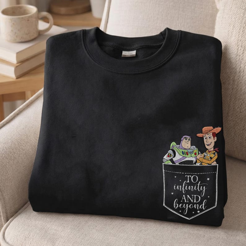 May include: A black crewneck sweatshirt featuring a graphic on the lower right side. The graphic depicts a pocket design with Buzz Lightyear and Woody characters above the white text "TO infinity AND beyond" with small star accents.