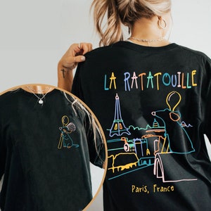 May include: Black t-shirt with a colorful graphic of Remy the rat from the movie Ratatouille, standing on a rooftop in Paris, France. The text "La Ratatouille" is above the graphic and "Paris, France" is below.