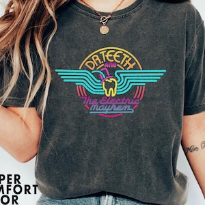 Puede incluir: Una camiseta negra con un gráfico colorido de un diente con un sombrero de copa y el texto "Dr. Teeth and the Electric Mayhem".