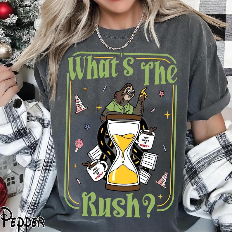 Puede incluir: Camiseta gris oscuro con un dise&ntilde;o gr&aacute;fico humor&iacute;stico. Presenta un perezoso, un reloj de arena y la frase "What's The Rush?". El dise&ntilde;o incluye tazas de caf&eacute; y elementos de carretera, con el texto "You want it when?" en las tazas.