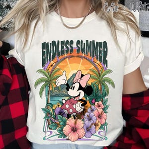 May include: White t-shirt featuring a colorful graphic of Minnie Mouse in a tropical setting. The design includes palm trees, flowers, and the text "ENDLESS SUMMER" in a stylized font. The shirt has short sleeves.
