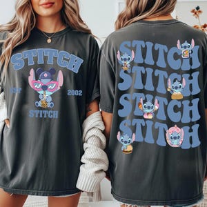 May include: Dark gray t-shirt featuring the word "STITCH" in light blue, with a cartoon character wearing sunglasses and holding a drink. The back of the shirt repeats "STITCH" with different Stitch illustrations.