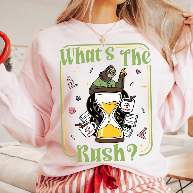 Puede incluir: Sudadera rosa claro con un dise&ntilde;o gr&aacute;fico humor&iacute;stico. Presenta un perezoso, un reloj de arena y la frase "What's The Rush?". El dise&ntilde;o incluye tazas de caf&eacute; y elementos de carretera.