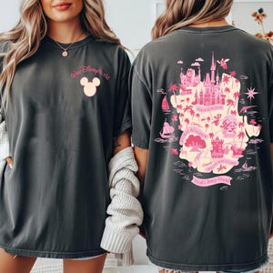 May include: Dark gray t-shirts with a pink Disney World design. The front features the words "Walt Disney World" above a Mickey Mouse head. The back displays a map of the Magic Kingdom and other parks in pink.