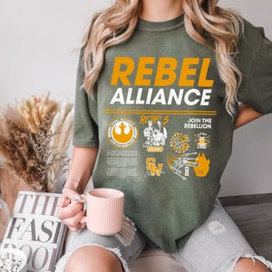 May include: A green t-shirt with the text "Rebel Alliance" in white and orange. The shirt features a variety of Star Wars themed graphics, including the Rebel Alliance symbol, the Millennium Falcon, and the words "Join the Rebellion".