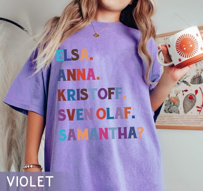 以下が含まれることがあります： エルサ、アナ、クリストフ、スヴェン、オラフ、サマンサの名前が様々な色でプリントされた紫色のTシャツ。「VIOLET」の文字がシャツの下部にプリントされています。
