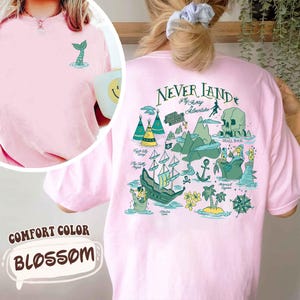 May include: Pale pink comfort colour t-shirt with a teal mermaid tail graphic. The back displays a teal and green Neverland map design with text. The shirt is labelled "Blossom".