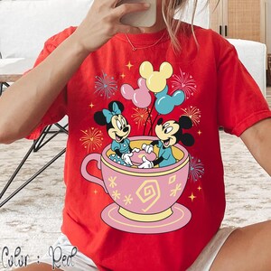 May include: Red t-shirt with a graphic of Mickey and Minnie Mouse in a teacup, holding balloons. The design includes fireworks and the text "Color: Red". The teacup is pink with yellow accents.