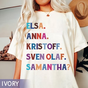 以下が含まれることがあります： アイボリー色のTシャツ。エルサ、アナ、クリストフ、スヴェン・オラフ、サマンサ？の名前がカラフルなブロック体でプリントされています。ゆったりとしたフィット感で、クルーネックです。「IVORY」の文字が下にプリントされています。