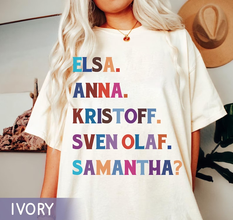 以下が含まれることがあります： アイボリー色のTシャツ。エルサ、アナ、クリストフ、スヴェン・オラフ、サマンサ？の名前がカラフルなブロック体でプリントされています。ゆったりとしたフィット感で、クルーネックです。「IVORY」の文字が下にプリントされています。