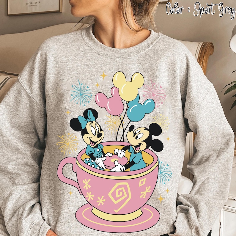 May include: Sport grey sweatshirt with a graphic of Mickey and Minnie Mouse in a pink teacup, holding a plate. The design includes balloons and fireworks, with the text "Color: Sport Grey".