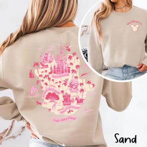 May include: Sand-colored sweatshirt featuring a pink graphic of the Walt Disney World map on the back. The design includes the Magic Kingdom castle, Animal Kingdom, and Hollywood Studios. The front has a small pink Mickey Mouse head and "Walt Disney World" text.