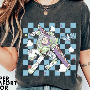 May include: A black t-shirt with a graphic print of Buzz Lightyear from Toy Story. The graphic features Buzz flying in a checkered pattern with clouds and stars. The text "More Ocean" is visible on the right sleeve.