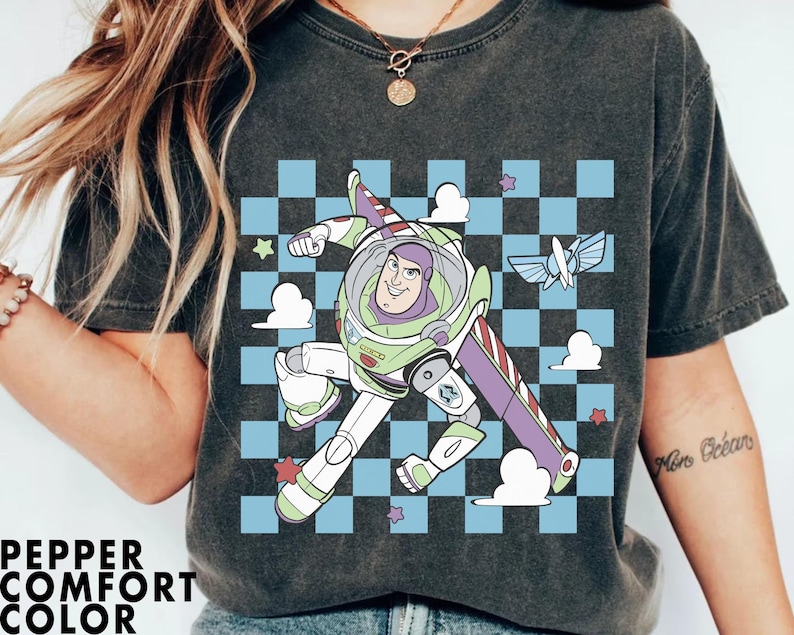 May include: A black t-shirt with a graphic print of Buzz Lightyear from Toy Story. The graphic features Buzz flying in a checkered pattern with clouds and stars. The text "More Ocean" is visible on the right sleeve.