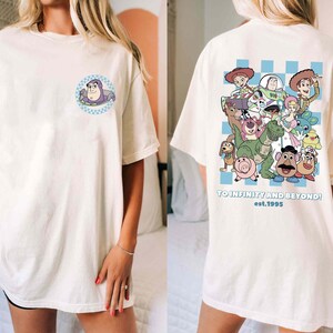 May include: White oversized t-shirt with a blue and white checkered pattern on the back. The back features a graphic of characters from the Toy Story movie franchise. The text "TO INFINITY AND BEYOND! est. 1995" is printed below the graphic. The front of the shirt features a small graphic of the character Buzz Lightyear.