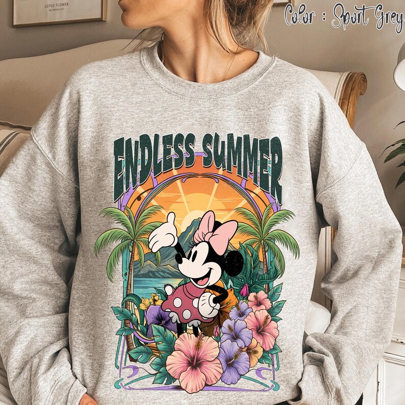 May include: Sport grey sweatshirt featuring a colorful graphic of Minnie Mouse in a pink polka dot dress, with the words "ENDLESS SUMMER" above her. The design includes palm trees, flowers, and a sunset scene. The sweatshirt is a comfortable, casual style.