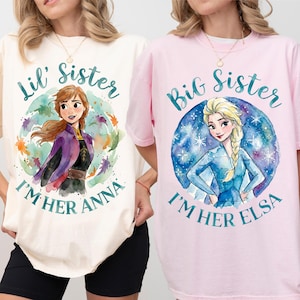 Könnte beinhalten: Zwei T-Shirts, eines in Creme und eines in Rosa, mit Aquarellillustrationen von Anna und Elsa aus Frozen. Das cremefarbene Shirt sagt "Lil' Sister, I'm Her Anna". Das rosa Shirt sagt "Big Sister, I'm Her Elsa".