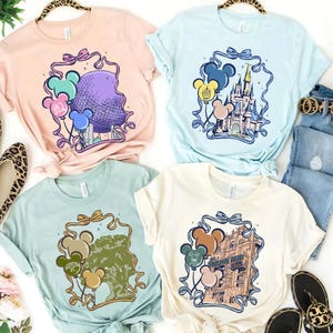 May include: Four pastel-colored t-shirts with Disney theme park graphics. Each shirt features a different park icon, including Spaceship Earth, Cinderella Castle, the Tree of Life, and the Tower of Terror, with Mickey Mouse balloon accents.