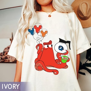 May include: A white t-shirt with a red octopus holding a blue fish in a glass jar. The octopus is holding balloons with Mickey Mouse ears. The text "IVORY" is at the bottom of the image.