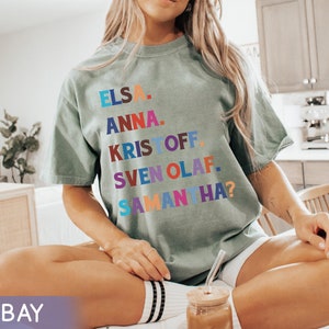 以下が含まれることがあります： エルサ、アナ、クリストフ、スヴェン、オラフ、サマンサ？の名前がカラフルなブロックレターでプリントされたセージグリーンのTシャツ。 ゆったりとしたフィット感で、半袖です。