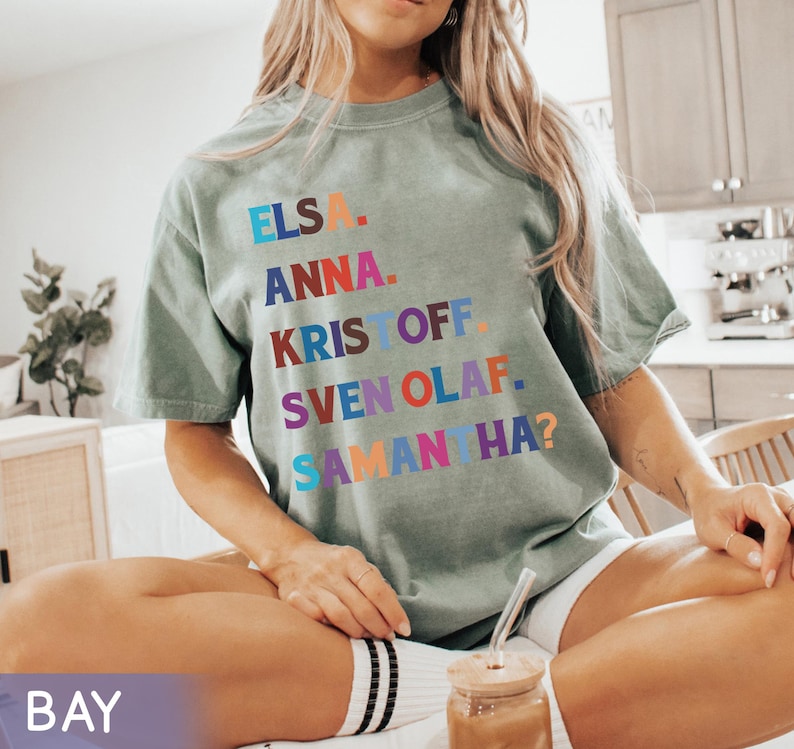 以下が含まれることがあります： エルサ、アナ、クリストフ、スヴェン、オラフ、サマンサ？の名前がカラフルなブロックレターでプリントされたセージグリーンのTシャツ。 ゆったりとしたフィット感で、半袖です。