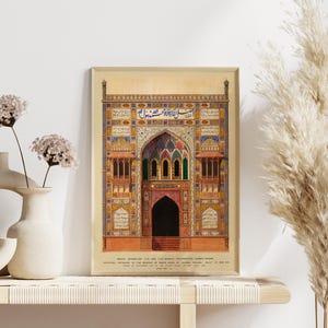 May include: A framed print of a detailed illustration of a colorful, ornate building with intricate details and Arabic script. The building has a large arched entrance with a doorway and a series of smaller windows. The print is set against a white wall with a vase of flowers and a dried grass plant on a shelf.