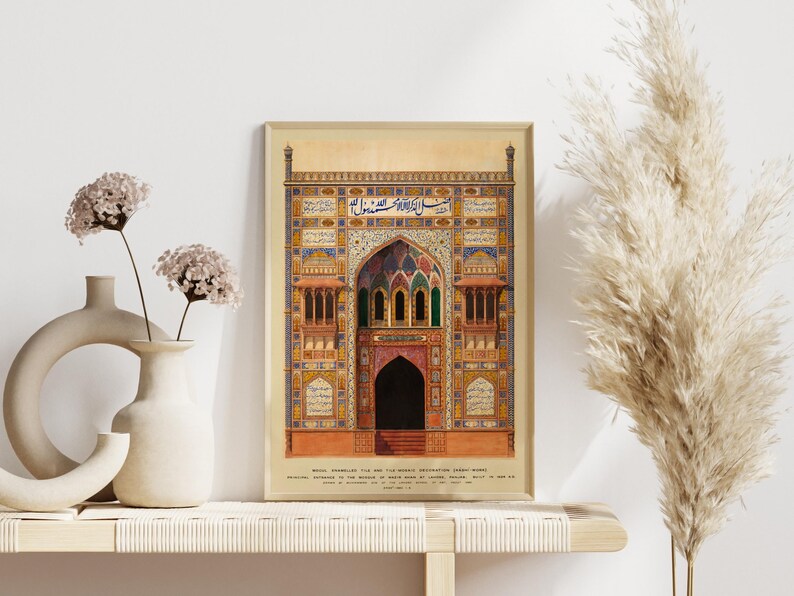 May include: A framed print of a detailed illustration of a colorful, ornate building with intricate details and Arabic script. The building has a large arched entrance with a doorway and a series of smaller windows. The print is set against a white wall with a vase of flowers and a dried grass plant on a shelf.