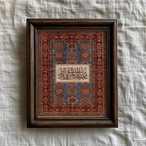May include: A framed artwork featuring a detailed rug design in shades of blue, red, and gold. The rug pattern serves as the background for a rectangular panel with Arabic calligraphy. The frame is a dark brown wood.