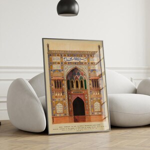 May include: A framed print of an intricate, colorful, and detailed illustration of an ornate archway with Arabic script. The archway is decorated with geometric patterns and floral motifs. The print is set against a white wall and a white couch.