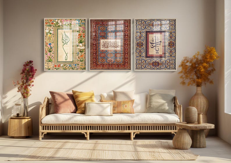 May include: Three framed art pieces with ornate designs and calligraphy hang above a white sofa with pillows. The art features floral and geometric patterns in shades of red, blue, and beige. A wooden side table and vase are in the foreground.