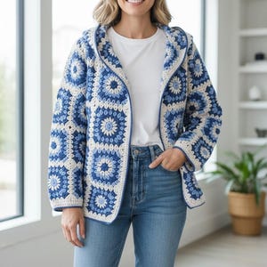 May include: A hooded cardigan constructed from crocheted granny squares in shades of navy blue, light blue, and cream. The garment features a floral-inspired pattern within each square, long sleeves, and a solid blue trim along the front opening.