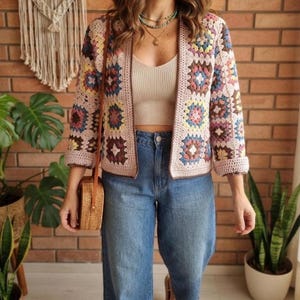 Könnte beinhalten: Eine langärmelige Häkeljacke mit einem mehrfarbigen Granny-Square-Muster in Rosa, Blau, Gelb und Braun, kombiniert mit einem beigen gerippten Tanktop, einer blauen Jeans und einer runden Umhängetasche aus geflochtenem Stroh mit braunem Riemen.