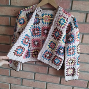 May include: A long-sleeved cardigan made of crocheted granny squares in various colors including pink, blue, yellow, and brown, joined together with light beige yarn. The garment features a brown crocheted border along the edges and cuffs.
