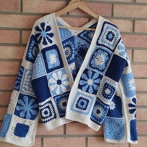 May include: A long-sleeved cardigan made from crocheted granny squares in shades of navy blue, light blue, and cream. The garment features a variety of square patterns, including floral motifs and geometric designs, joined together with cream yarn.
