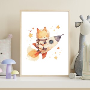 May include: Watercolor illustration of a fox astronaut in a spacesuit riding a rocket ship. The rocket is white and red, with orange flames. Yellow stars are scattered around the rocket. The artwork is framed in a light wood frame.