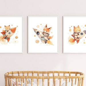May include: Set of three framed watercolor prints featuring a fox in a rocket ship. The fox is depicted in a spacesuit, surrounded by stars and planets. The rocket is orange and white, with a trail of smoke.