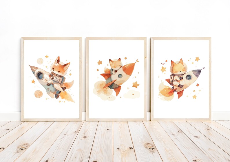 May include: Set of three framed watercolor art prints featuring foxes in space. Each print shows a fox astronaut riding a rocket ship, surrounded by stars and planets. The artwork has a soft, whimsical style with warm colors.